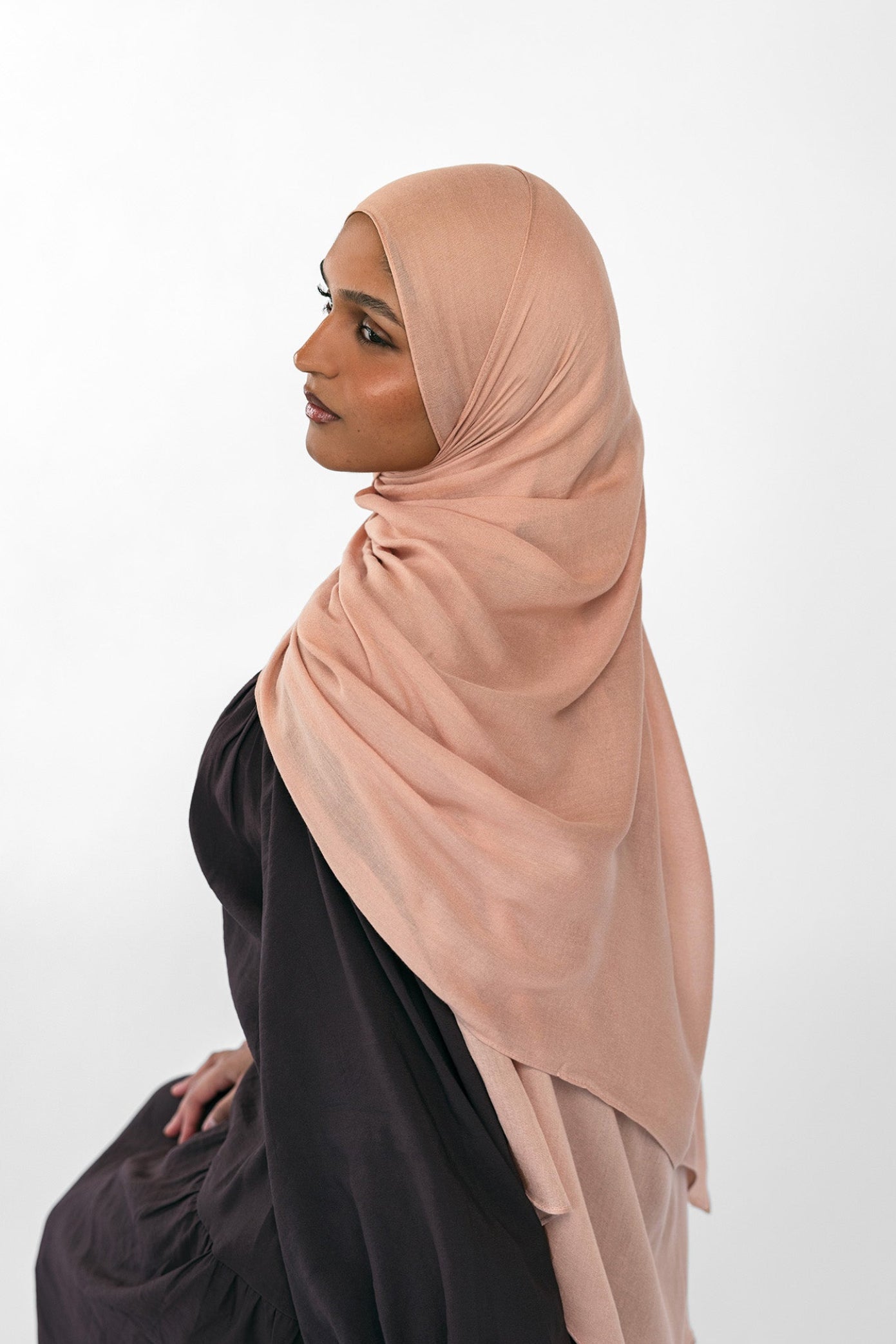 Woman wearing a beige hijab and black outfit on a white background