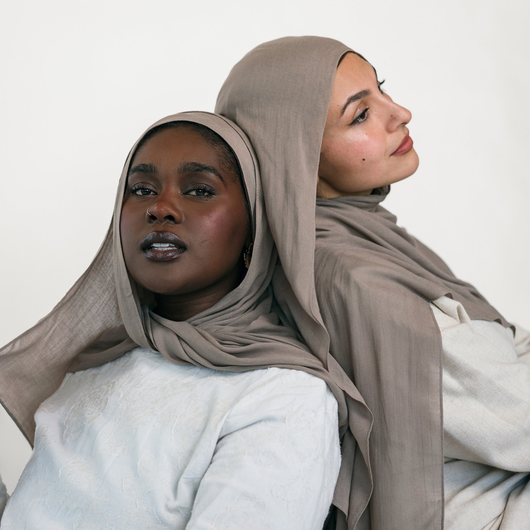 Two women wearing beige hijabs and light-colored clothing against a white background