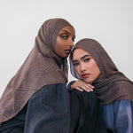Two women wearing brown striped hijabs and dark clothing against a white background