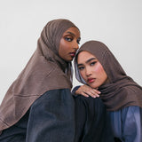 Two women wearing brown striped hijabs and dark clothing against a white background