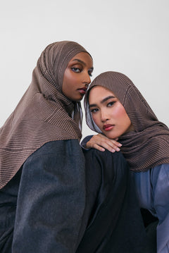 Two women wearing brown striped hijabs and dark clothing against a white background