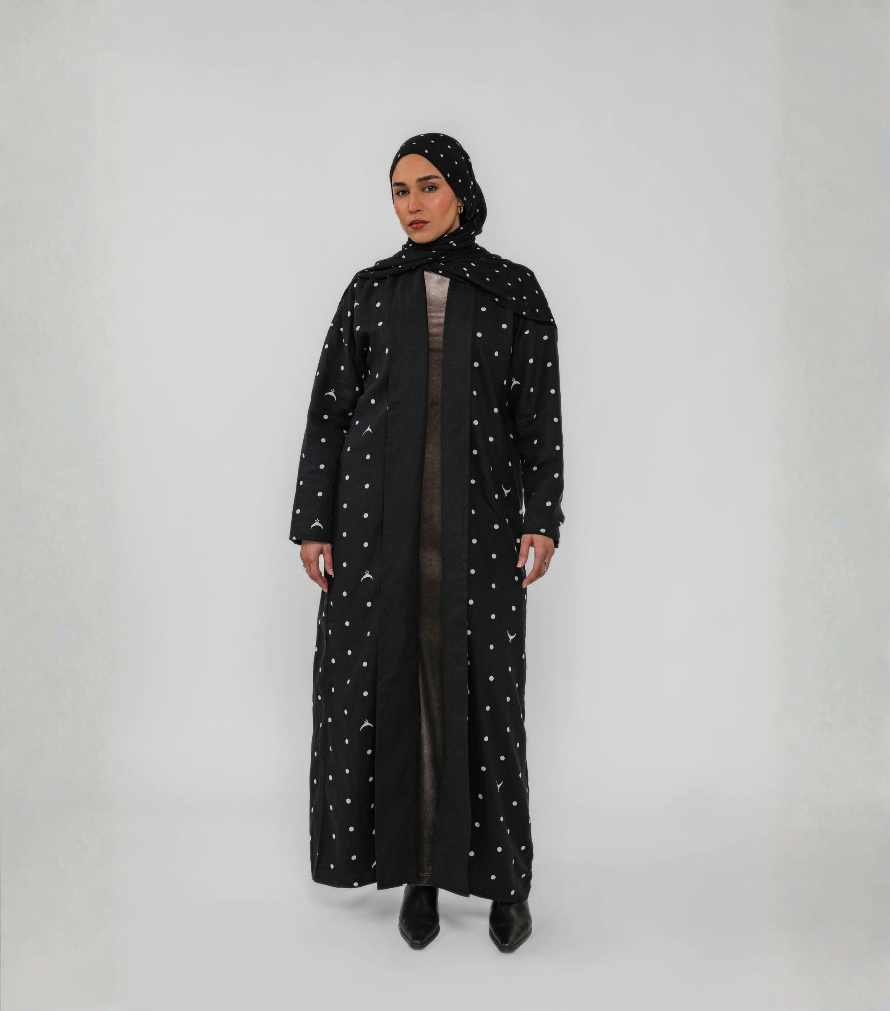 Woman wearing a long black abaya with white polka dots on a white background