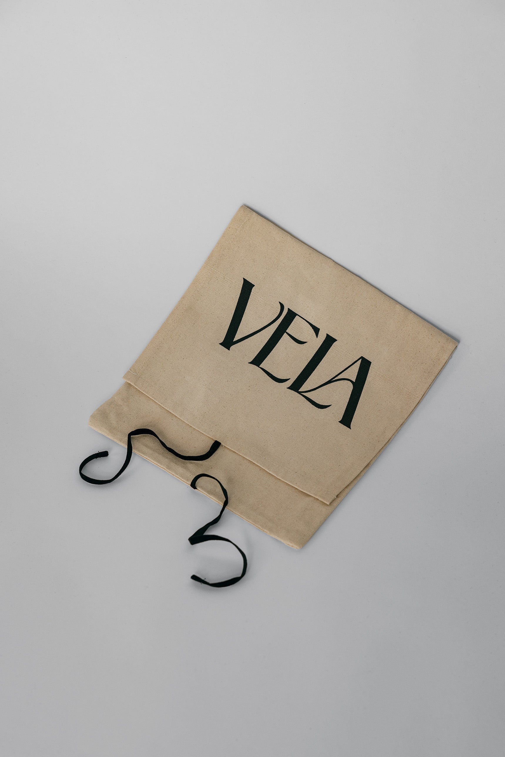 Beige drawstring bag with 'VELA' branding on a light gray background