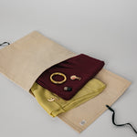 Folded maroon and yellow hijabs with charms on a beige drawstring bag against a light gray background