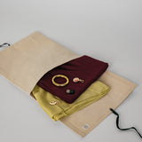 Folded maroon and yellow hijabs with charms on a beige drawstring bag against a light gray background