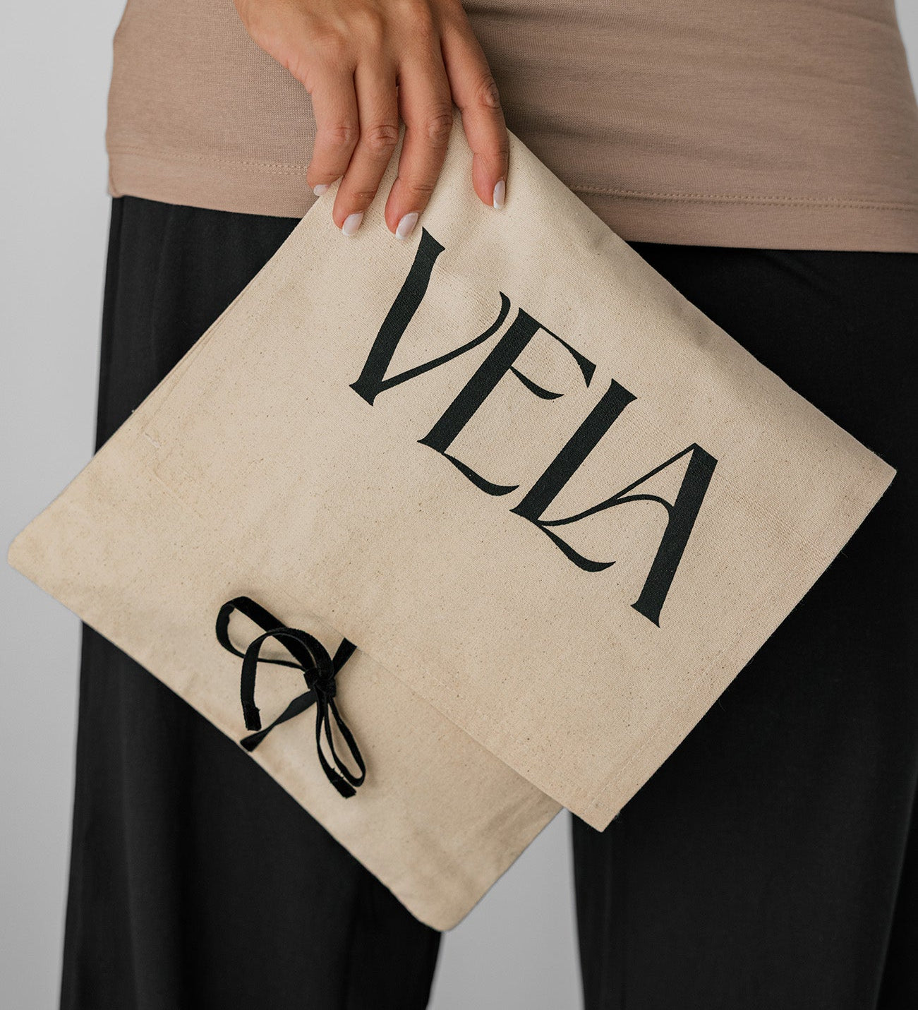 Person holding a beige pouch with 'Vela' branding against a neutral background