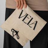 Person holding a beige pouch with 'Vela' branding against a neutral background