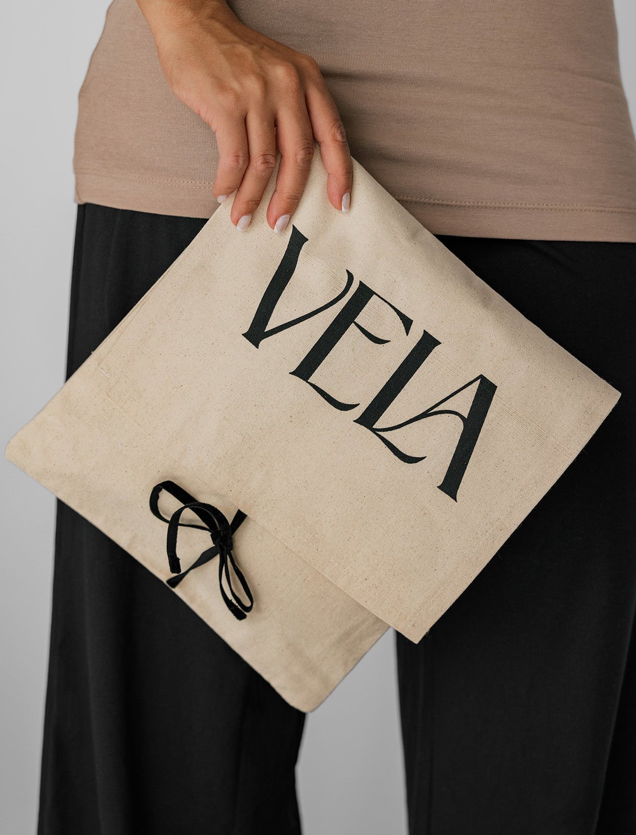 Person holding a beige pouch with 'Vela' branding against a neutral background