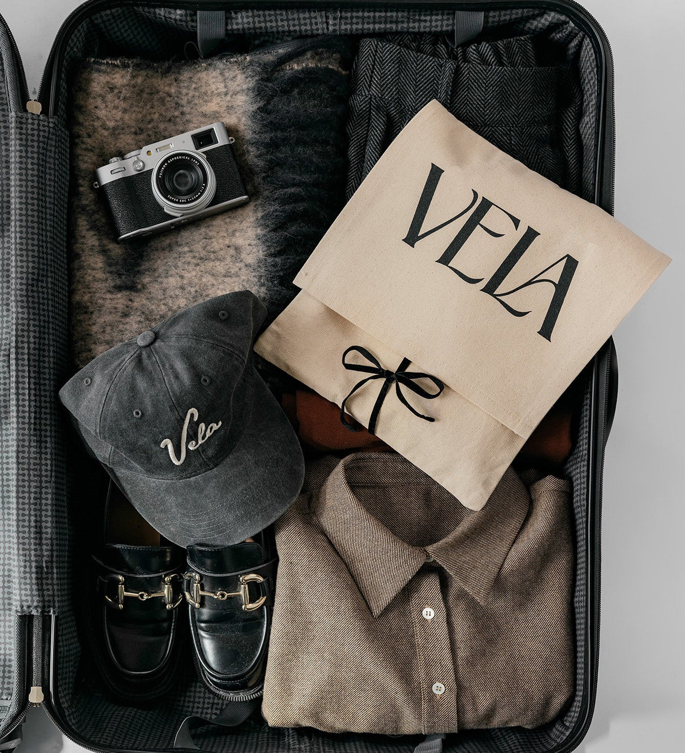 Open suitcase with clothing, a cap, and a camera on a light gray background