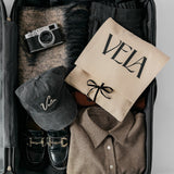 Open suitcase with clothing, a cap, and a camera on a light gray background