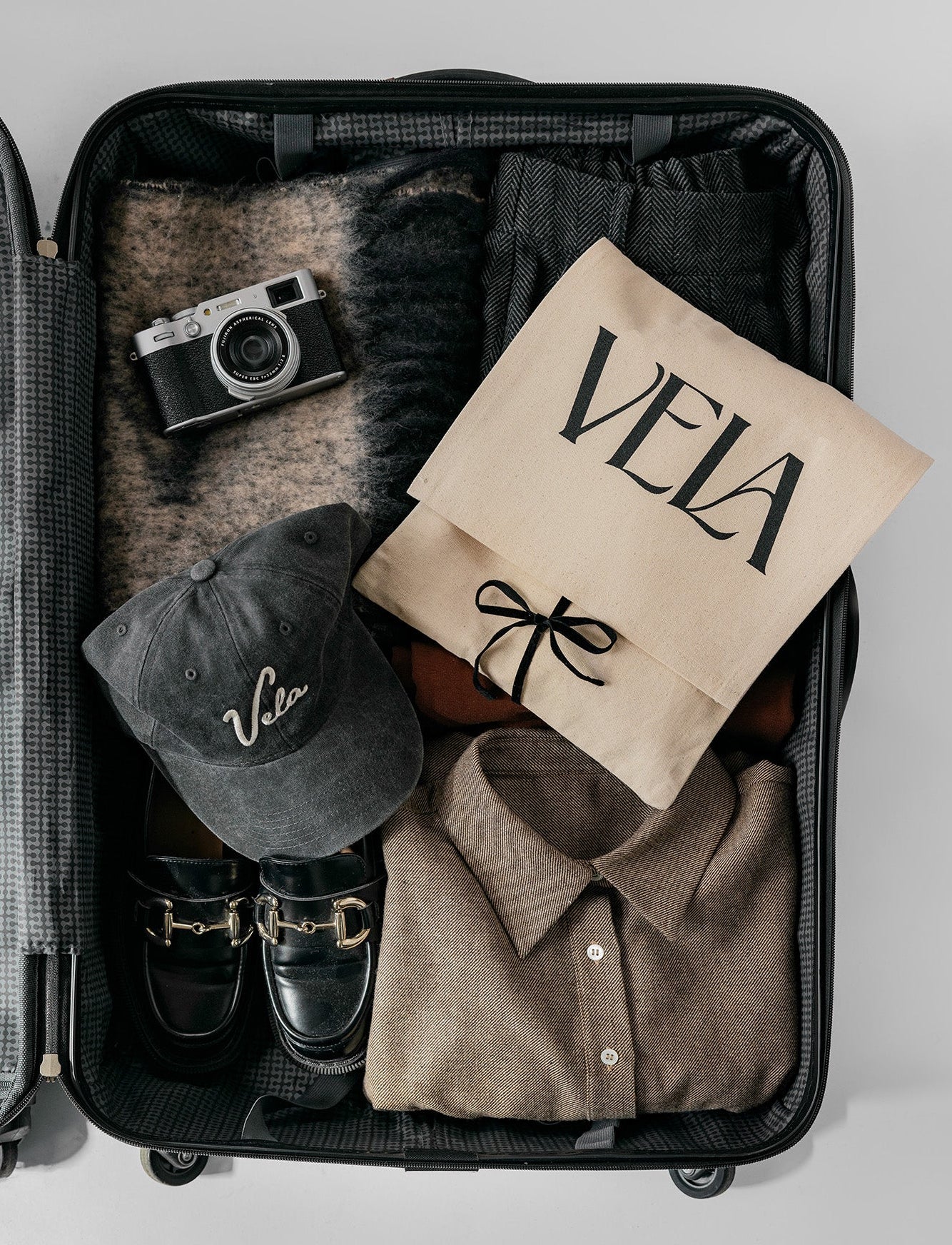 Open suitcase with clothing, a cap, and a camera on a light gray background