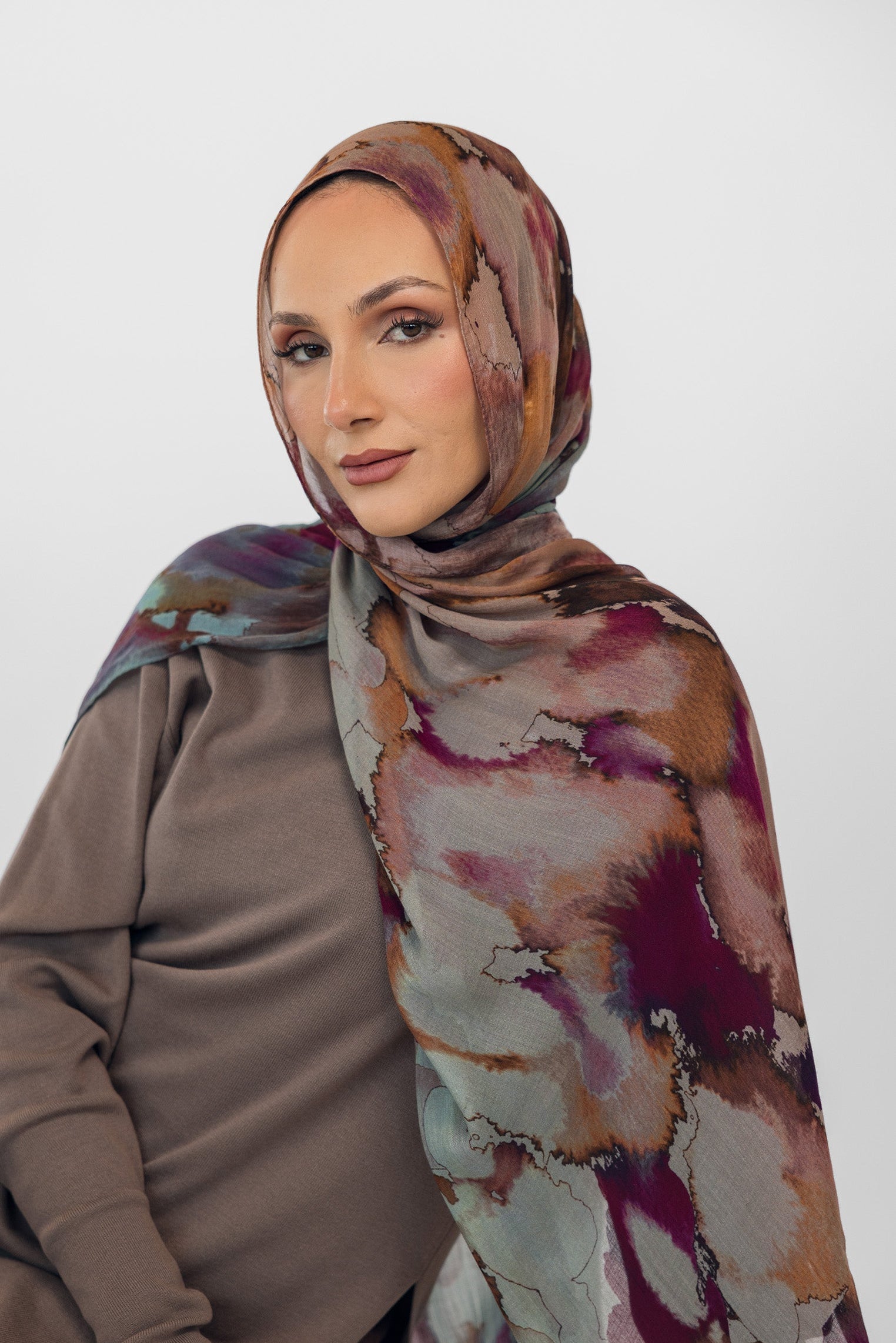 Woman wearing a watercolor floral patterned hijab and brown top against a white background