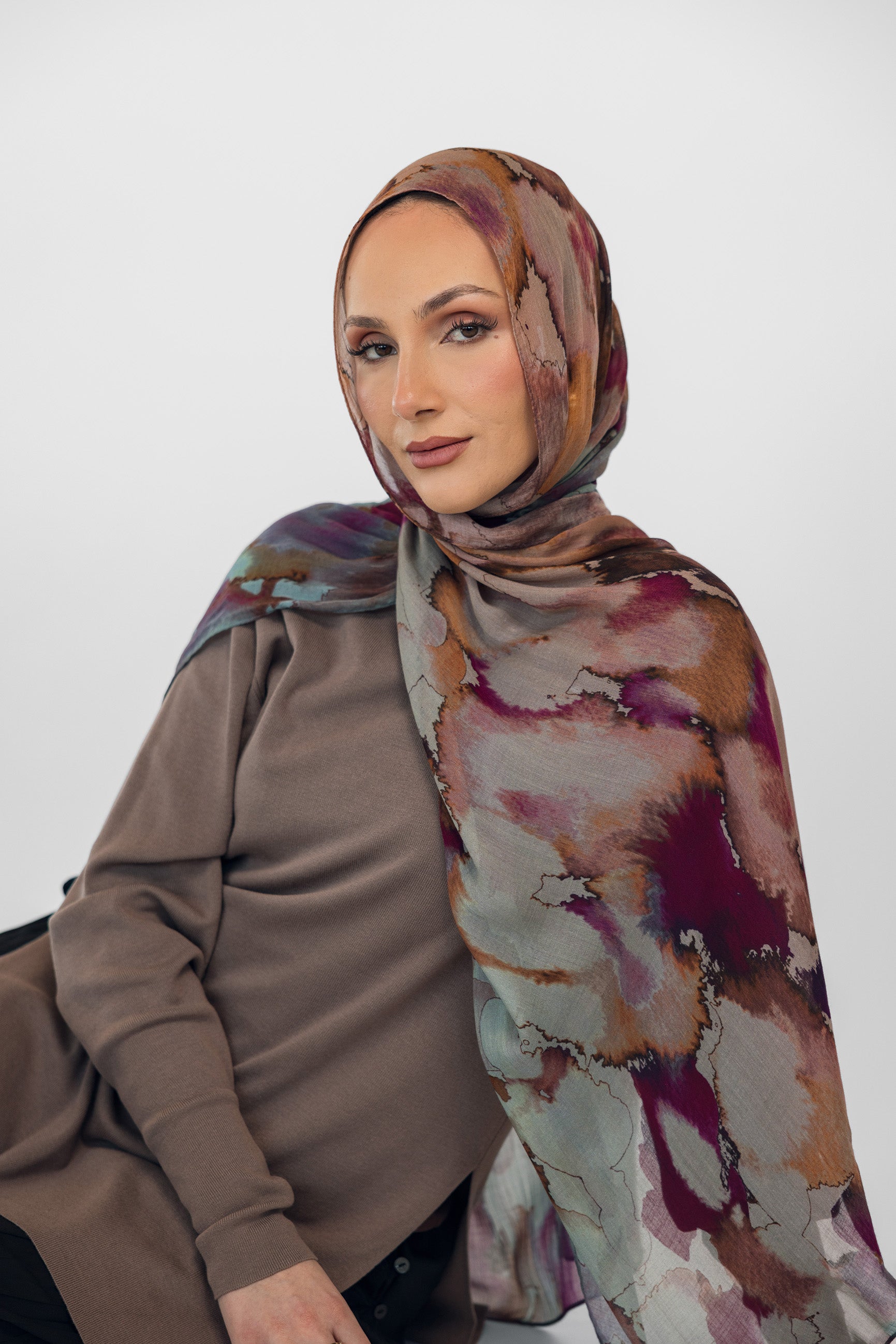 Woman wearing a watercolor floral patterned hijab and brown top against a white background
