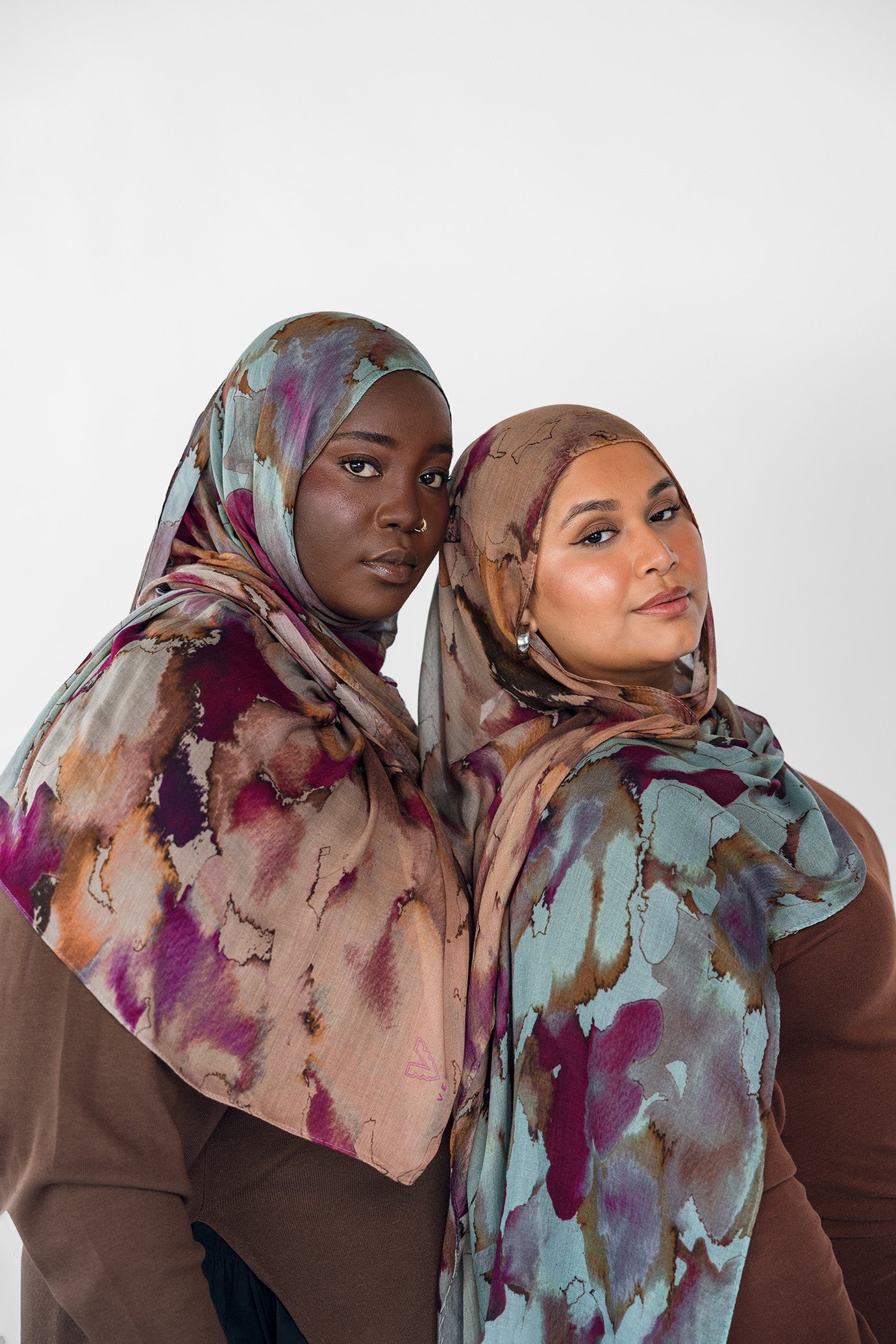 Two women wearing watercolor patterned hijabs against a white background