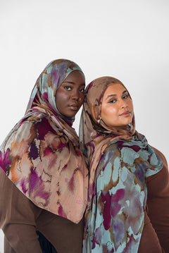 Two women wearing watercolor patterned hijabs against a white background