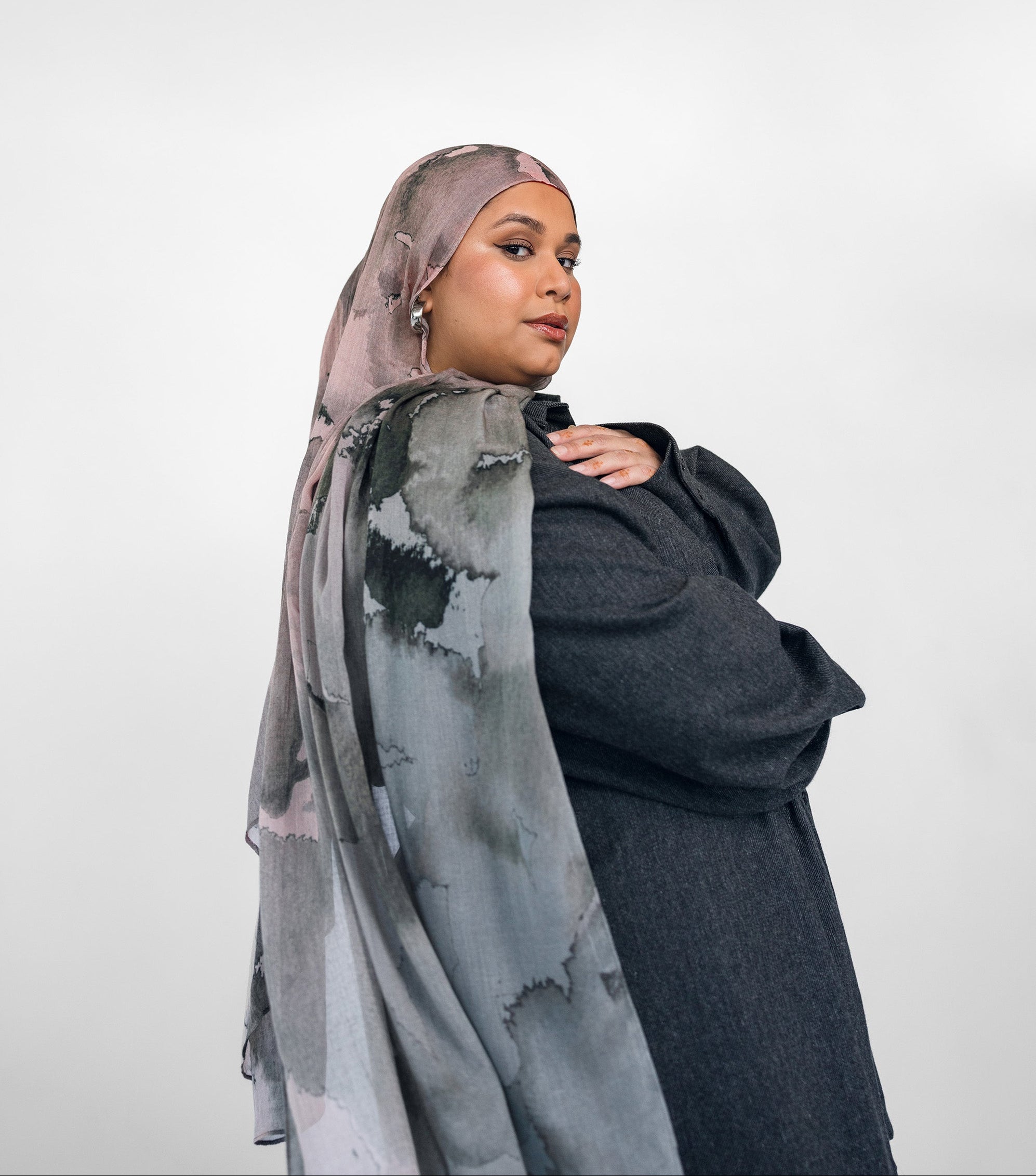 Woman wearing a gray and pink watercolor patterned hijab with a plain background