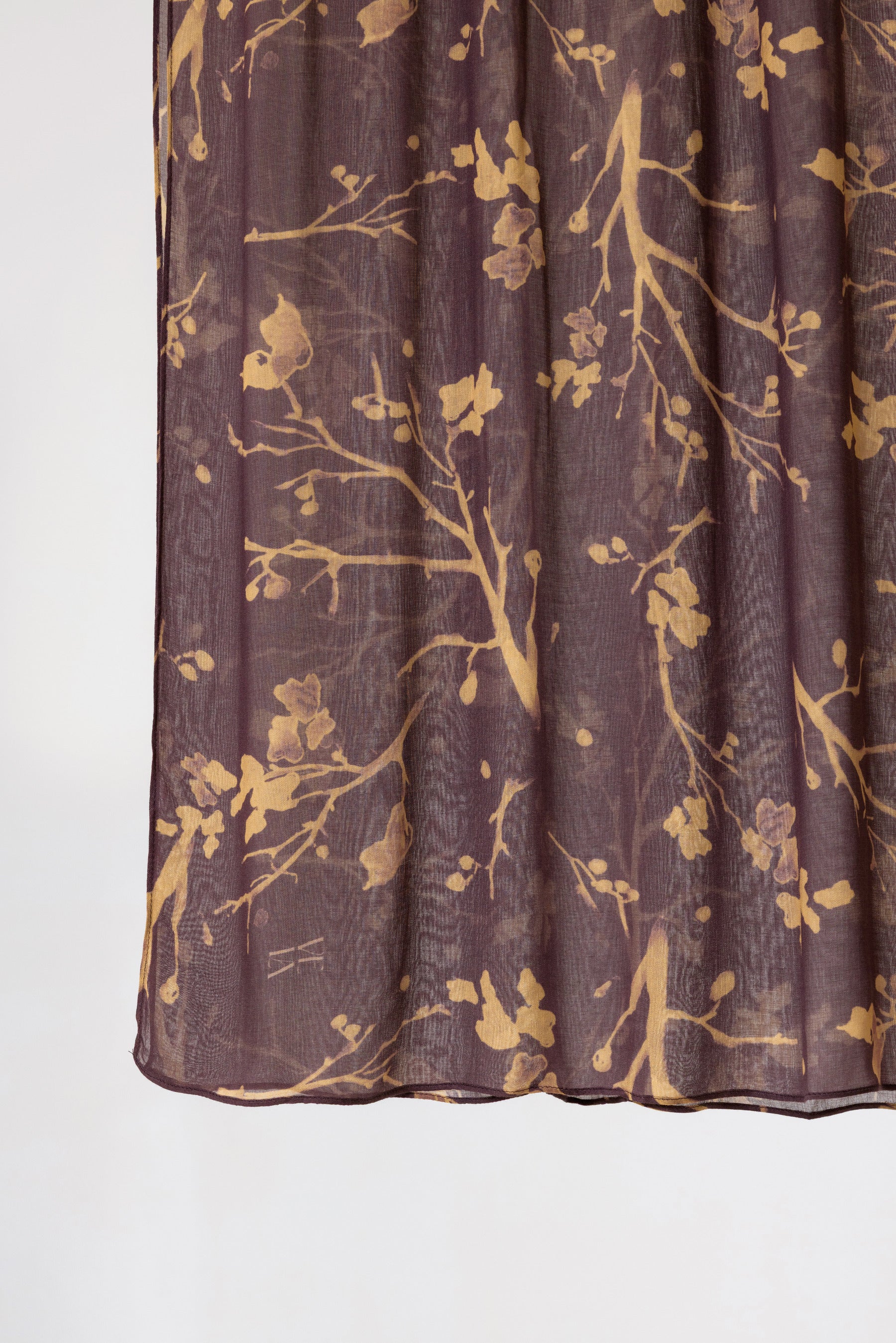A close-up of a sheer pleated fabric panel, likely a curtain, in a dark plum purple color with a metallic gold branch and floral pattern, shown against a plain white background.