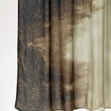 A sheer curtain panel with a mottled, abstract pattern in dark brown, charcoal gray, and beige, hanging against a plain white background.