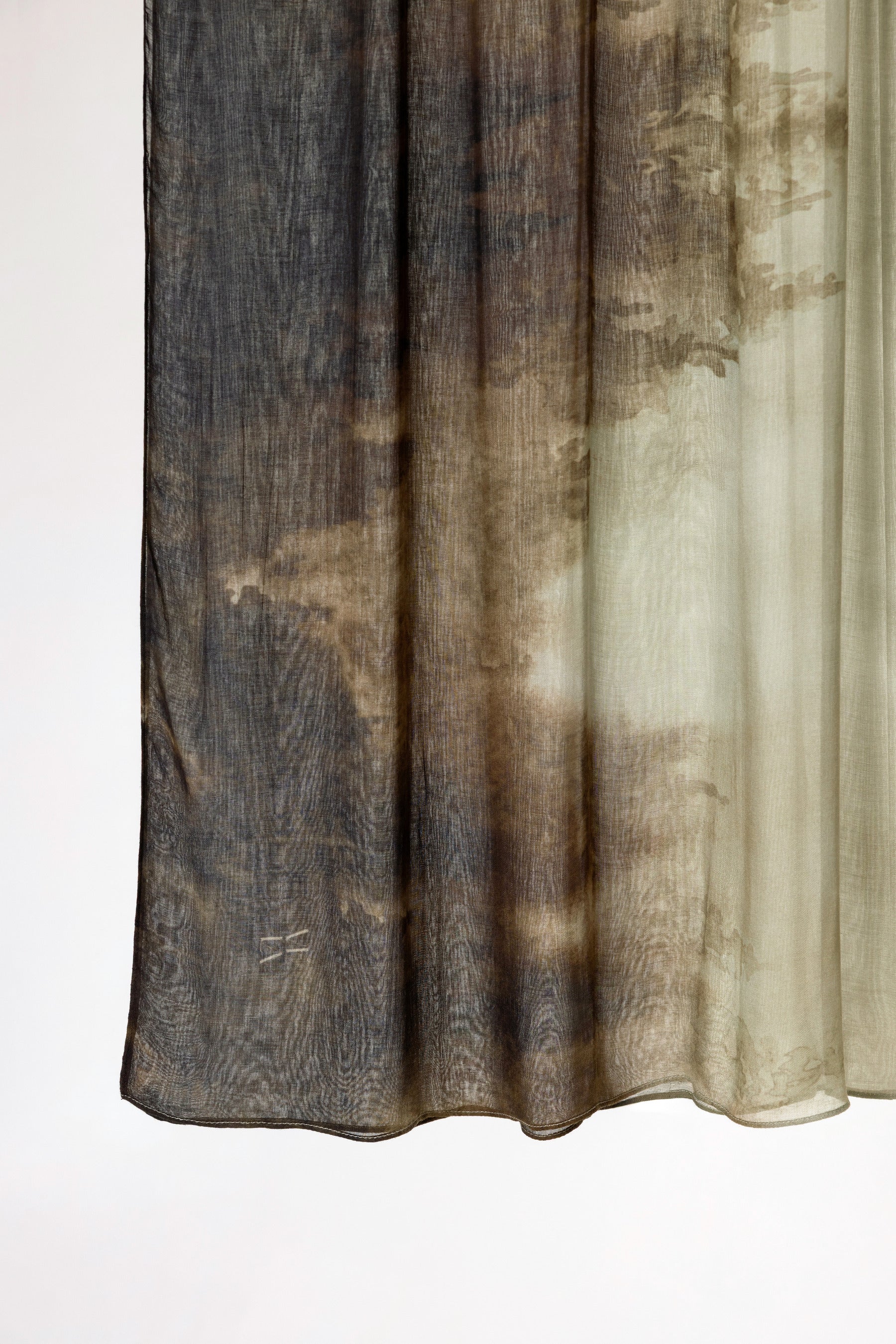 A sheer curtain panel with a mottled, abstract pattern in dark brown, charcoal gray, and beige, hanging against a plain white background.