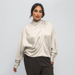 Woman wearing a beige long-sleeve top with a draped design on a white background