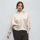 Woman wearing a beige long-sleeve top with a draped design on a white background