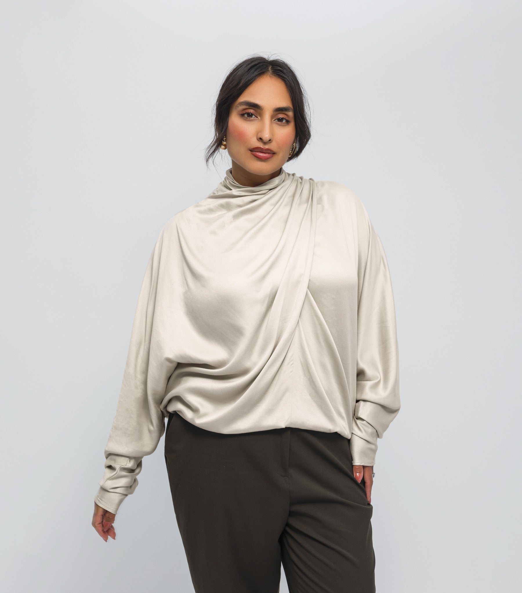 Woman wearing a beige long-sleeve top with a draped design on a white background