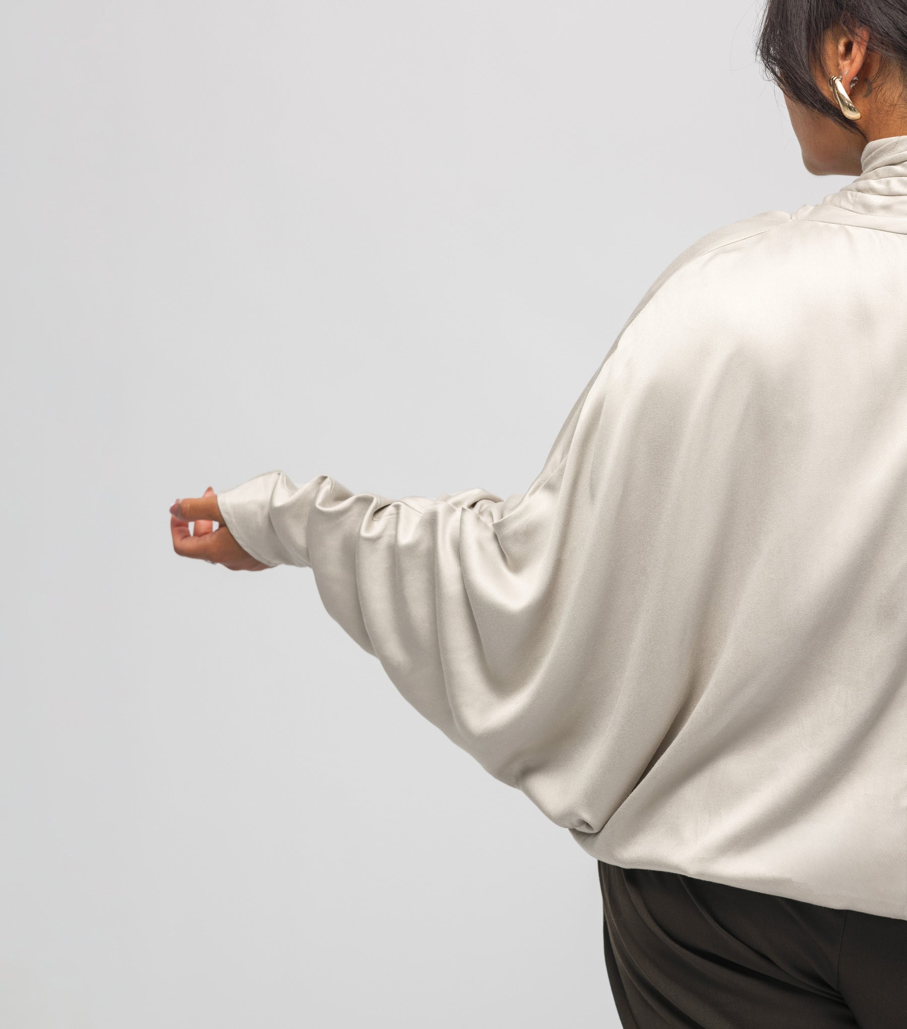 Person wearing a beige satin shirt on a light gray background