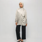 Woman wearing a beige hijab, long-sleeve top, and black pants on a white background
