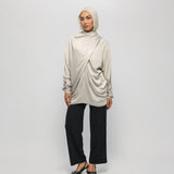 Woman wearing a beige hijab, long-sleeve top, and black pants on a white background