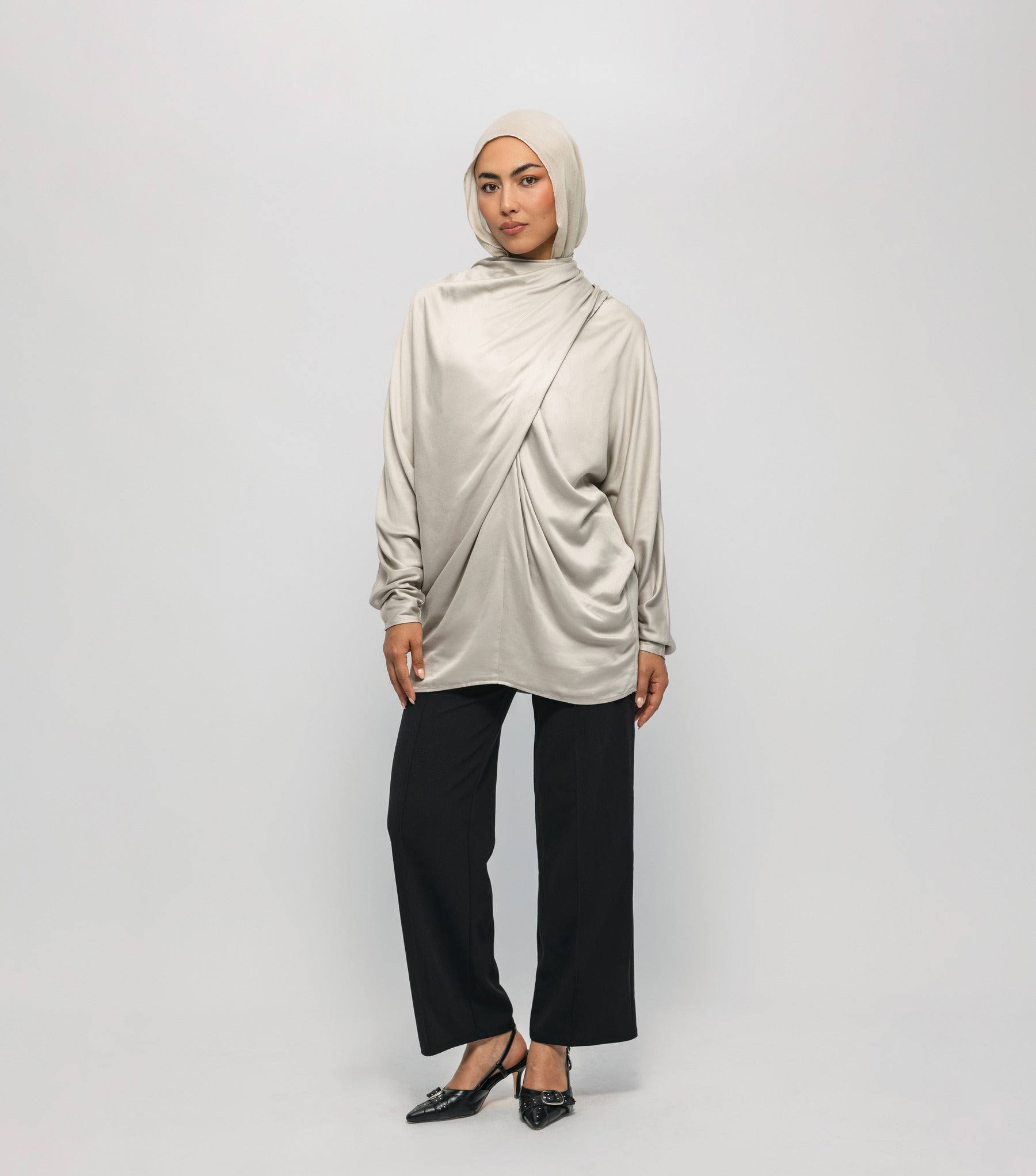 Woman wearing a beige hijab, long-sleeve top, and black pants on a white background