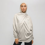 Woman wearing a beige hijab and long-sleeve top against a white background
