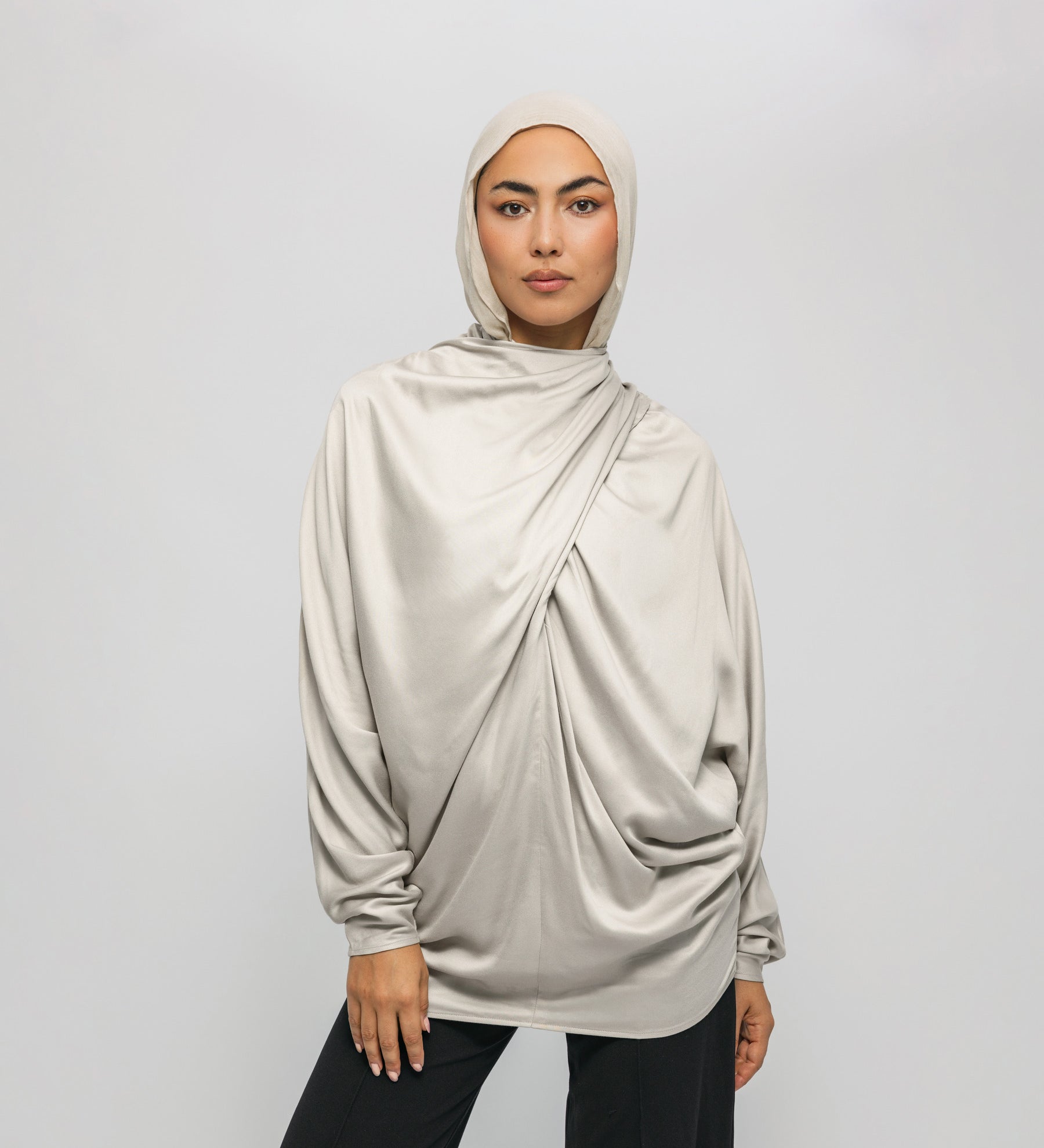 Woman wearing a beige hijab and long-sleeve top against a white background
