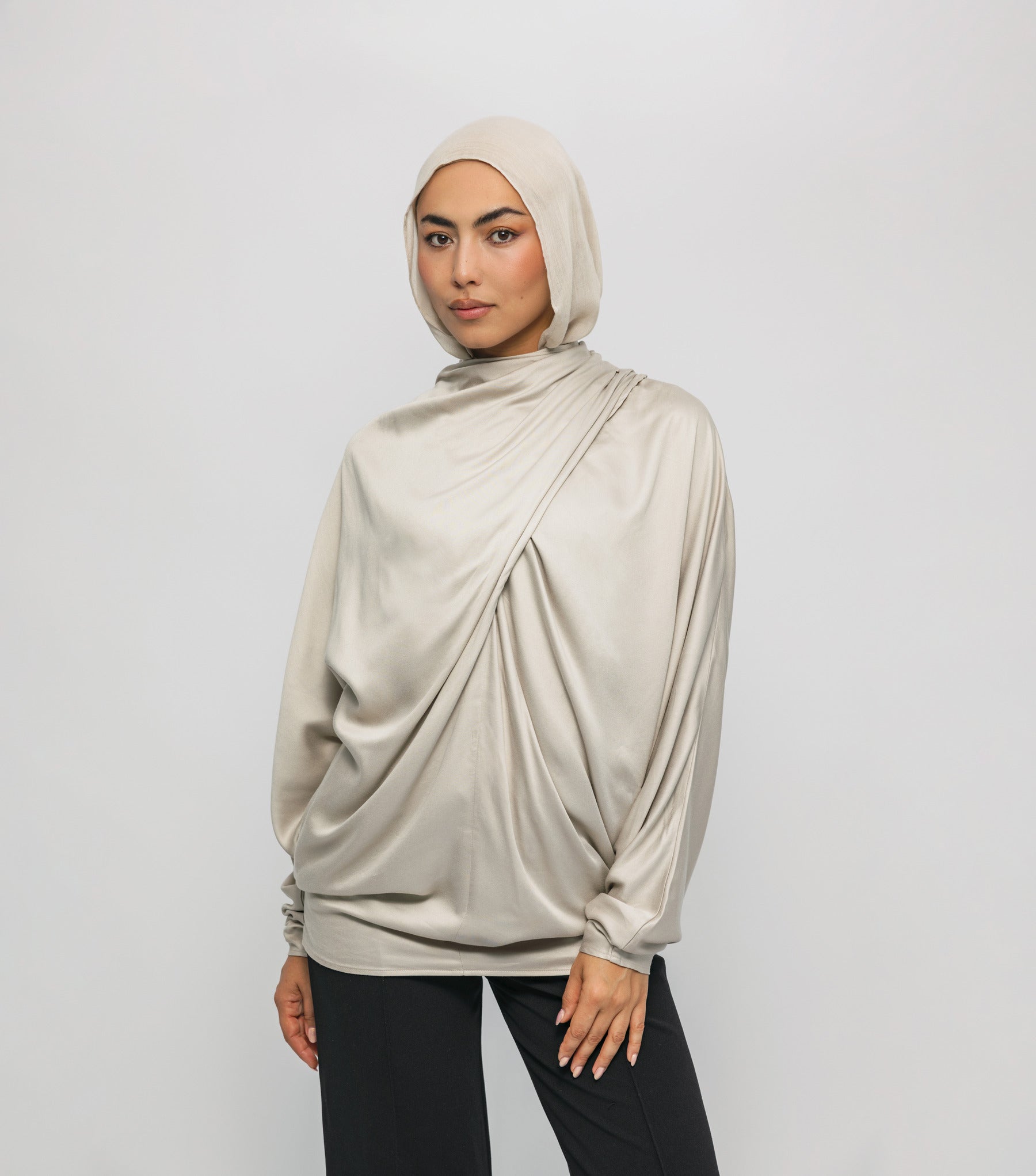 Woman wearing a beige hijab and top against a white background