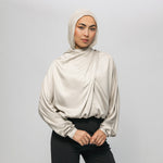 Woman wearing a beige hijab and blouse against a plain background