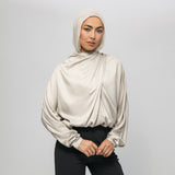 Woman wearing a beige hijab and blouse against a plain background