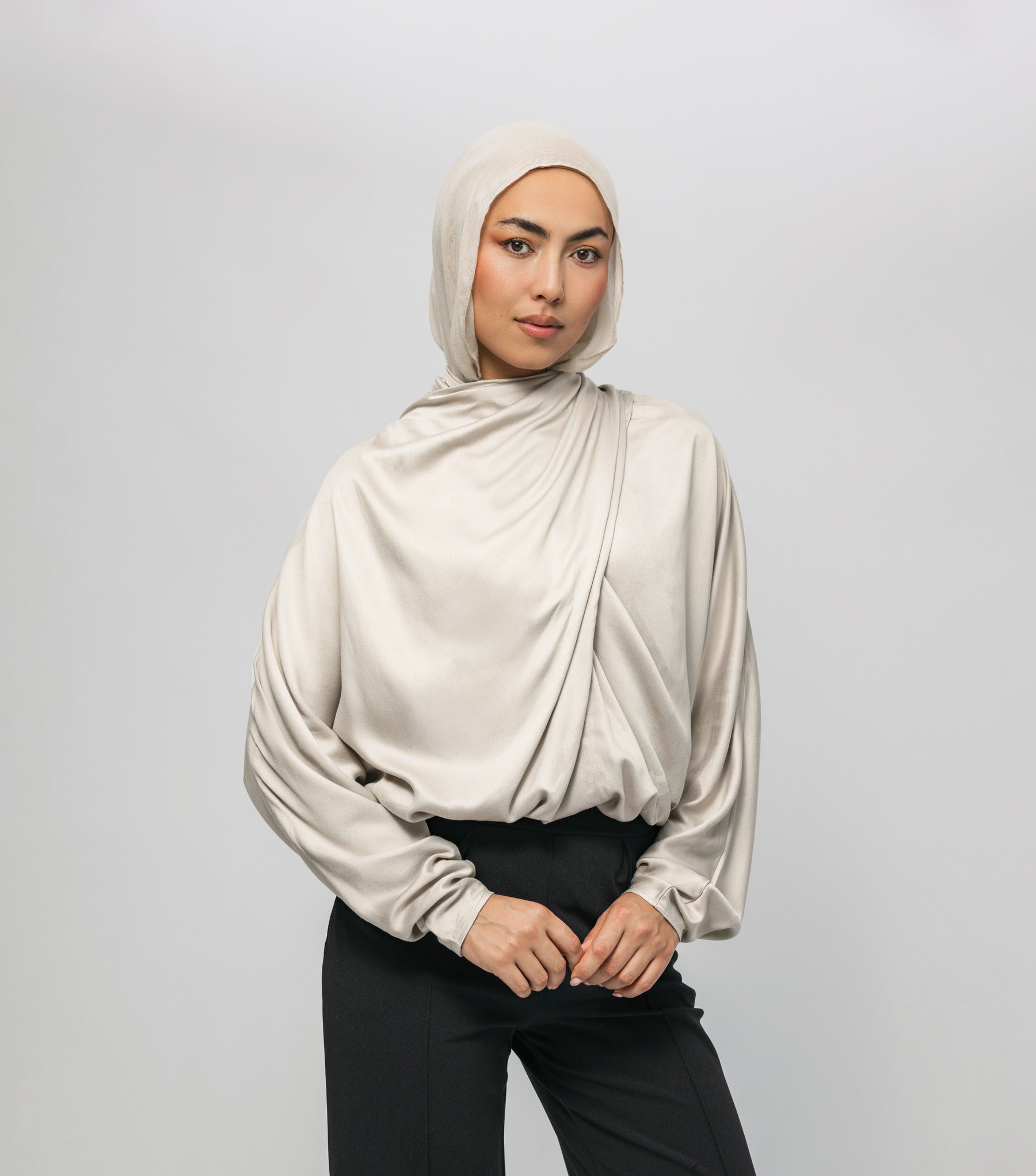 Woman wearing a beige hijab and blouse against a plain background