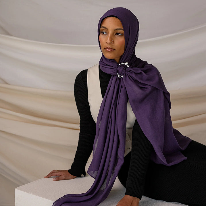 Woman wearing a purple hijab and scarf against a neutral background
