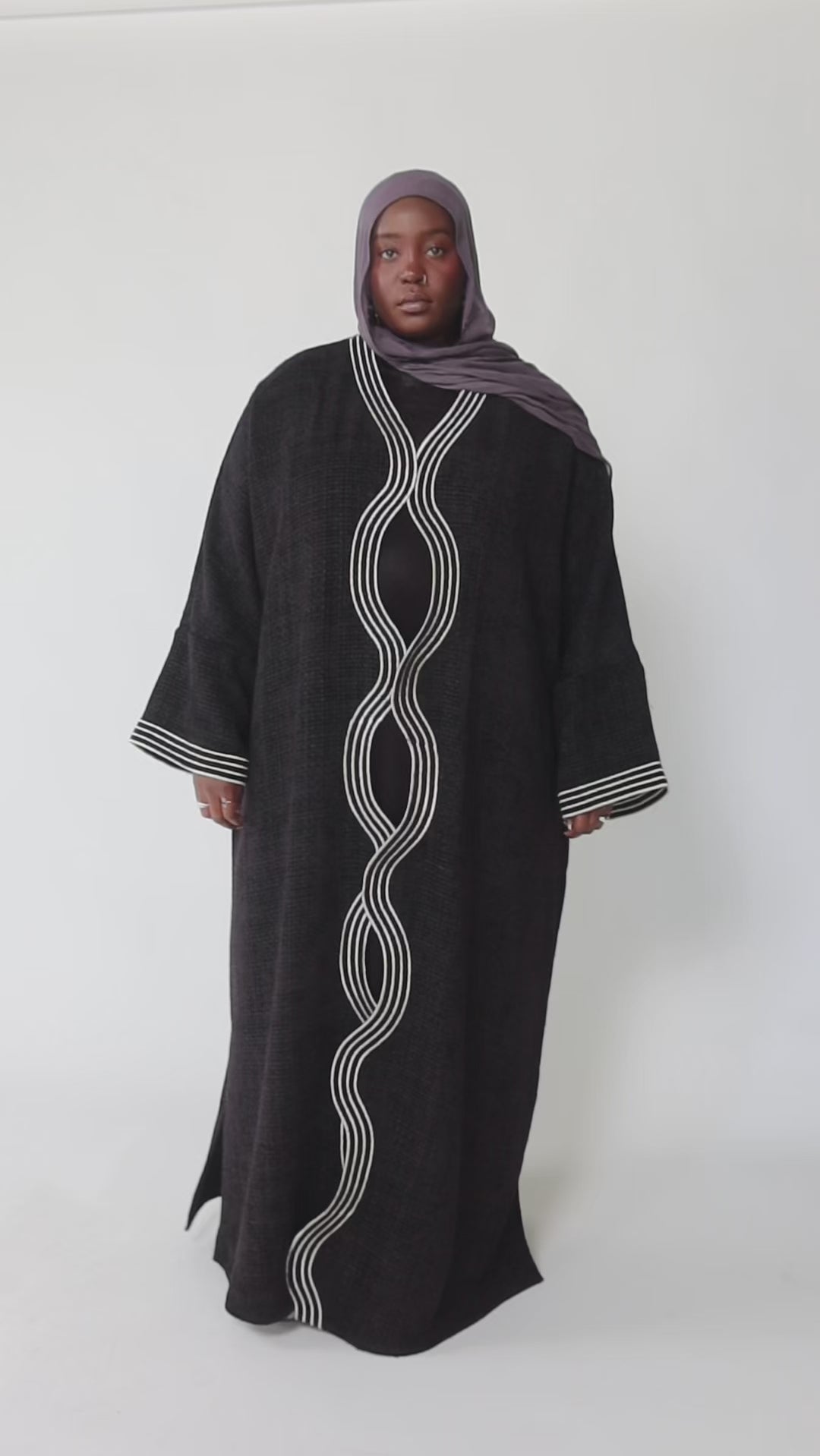 Woman wearing a black abaya with white embroidery on a white background