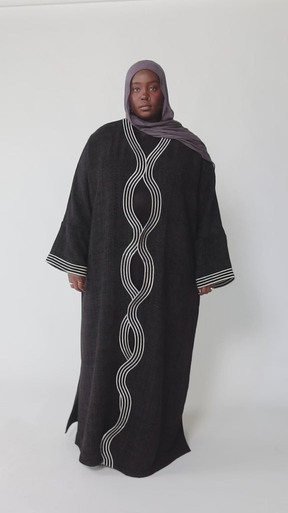 Woman wearing a black abaya with white embroidery on a white background