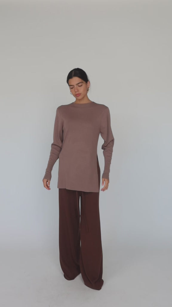 Model styled in long sleeve beige top with brown pants.