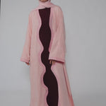Woman wearing a pink abaya with a black dress underneath on a white background