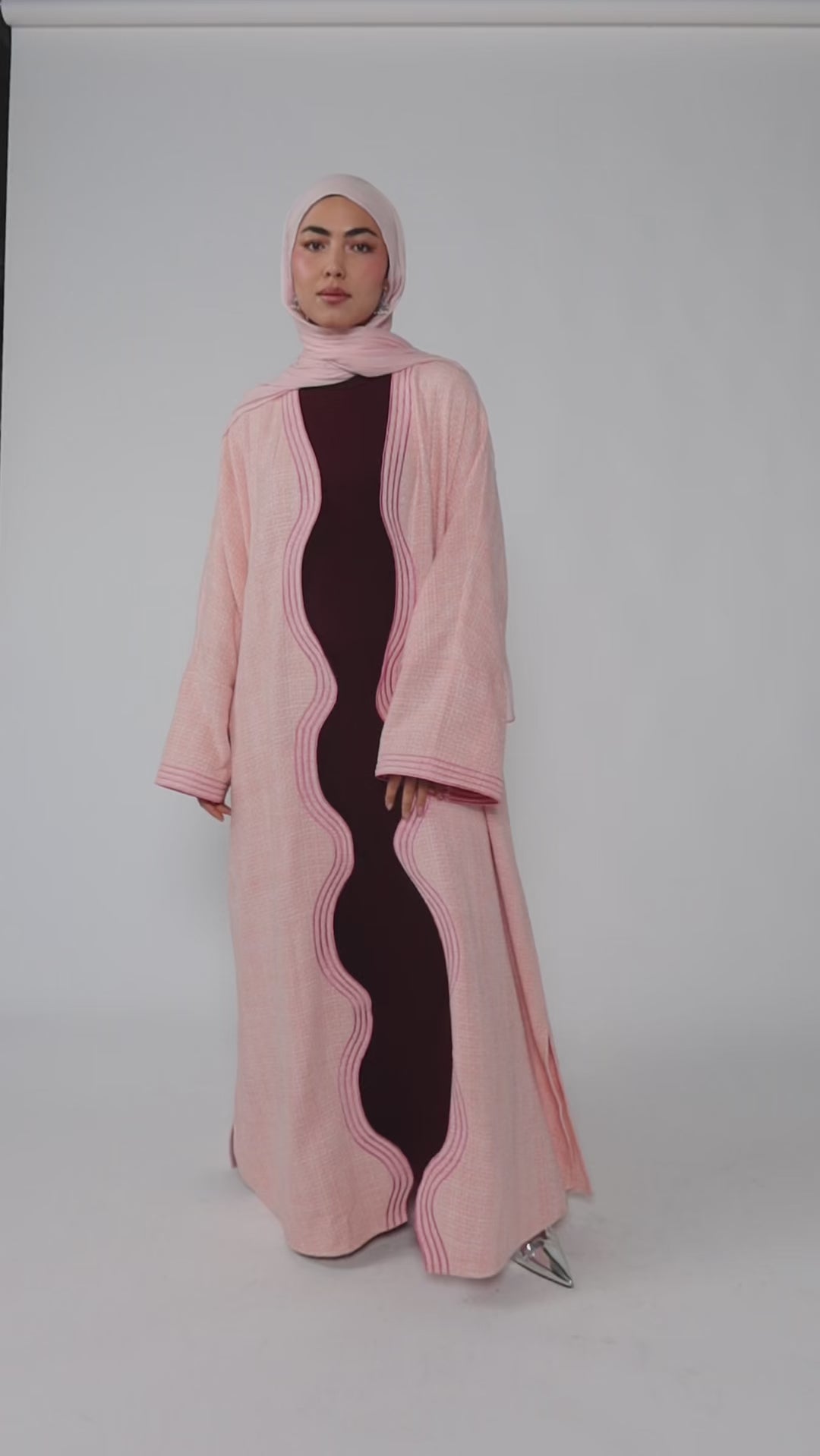 Woman wearing a pink abaya with a black dress underneath on a white background