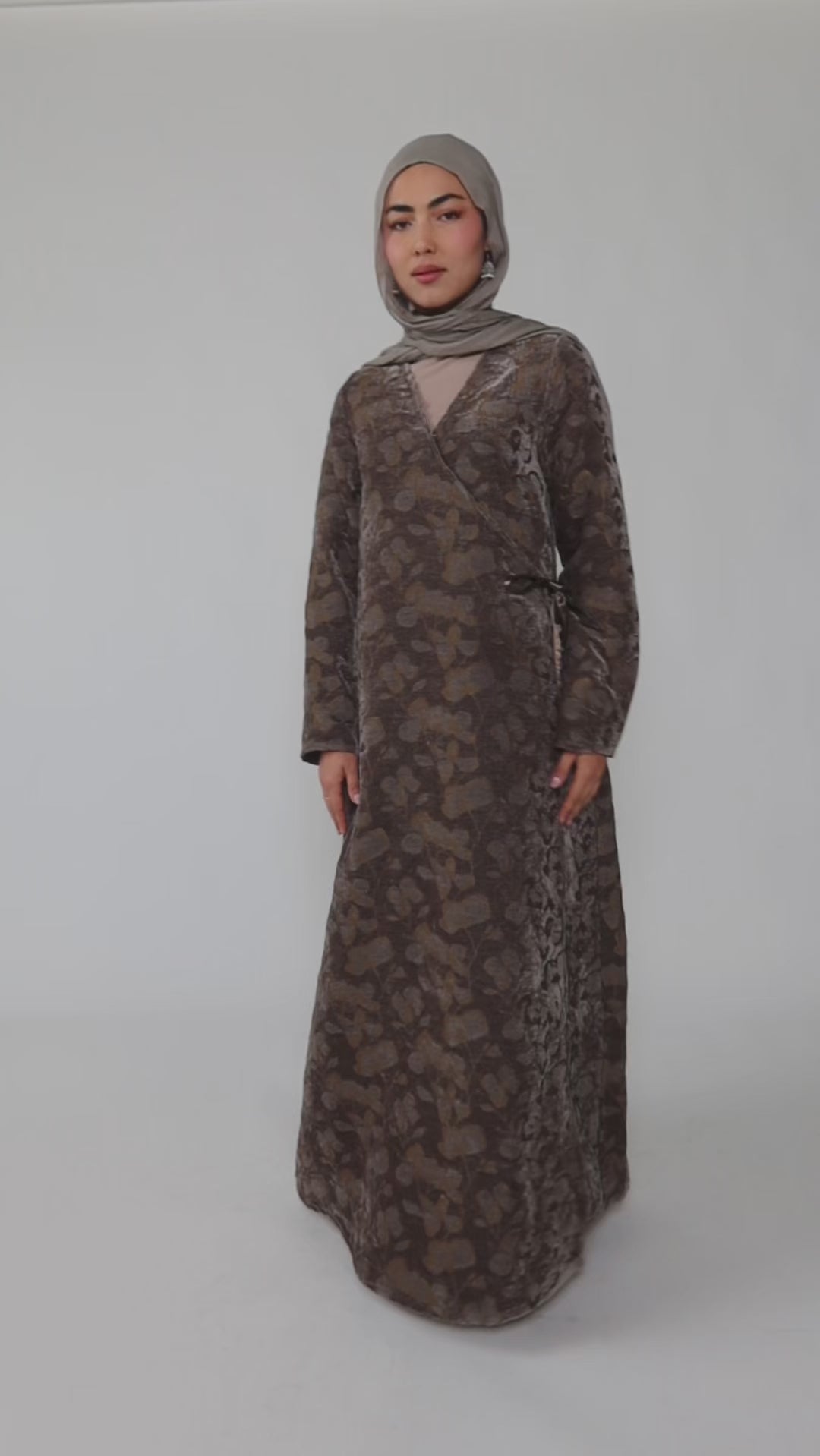 Woman wearing a green jacquard patterned abaya on a gray background