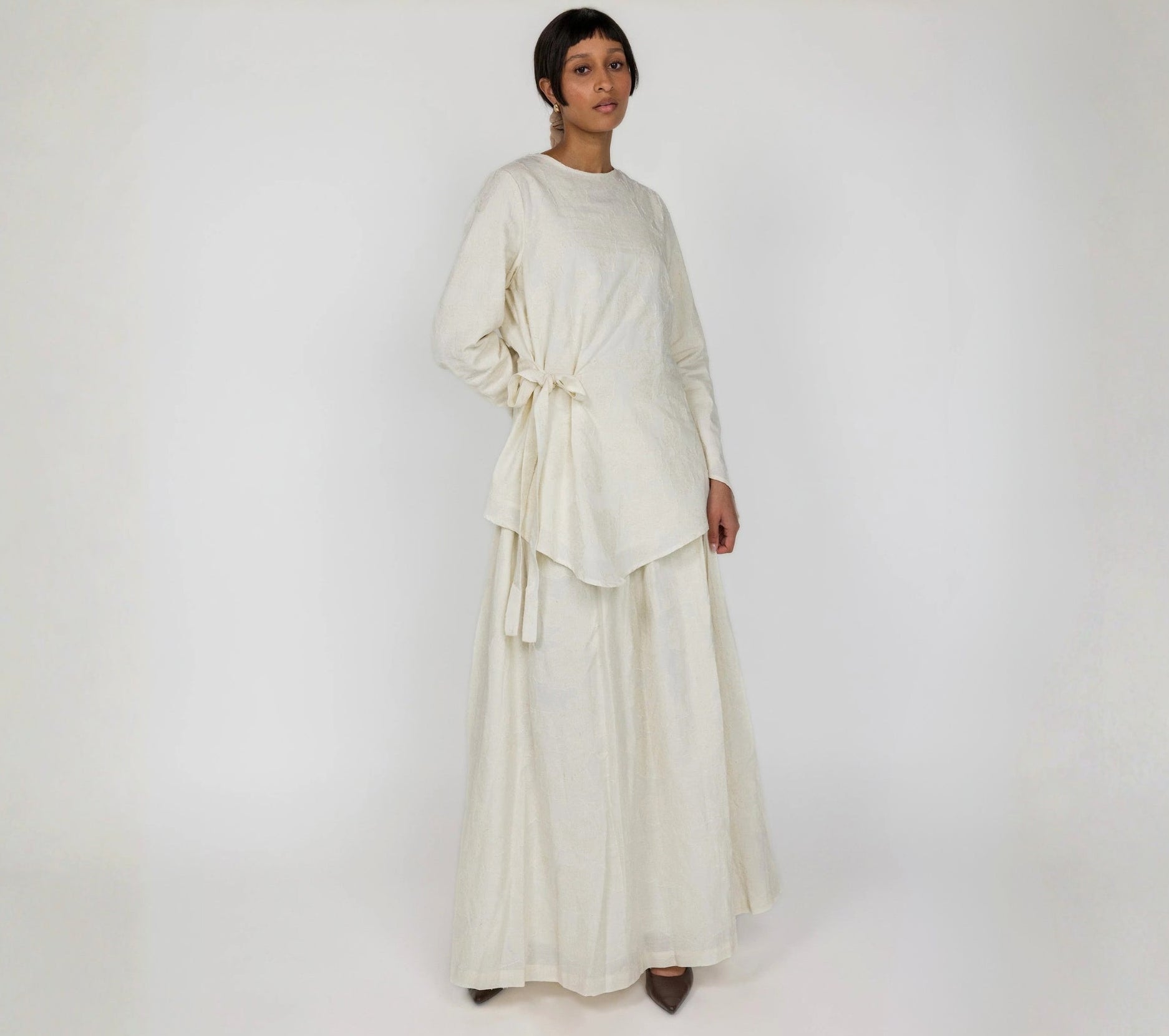 Woman wearing a white skirt and white top against a plain background
