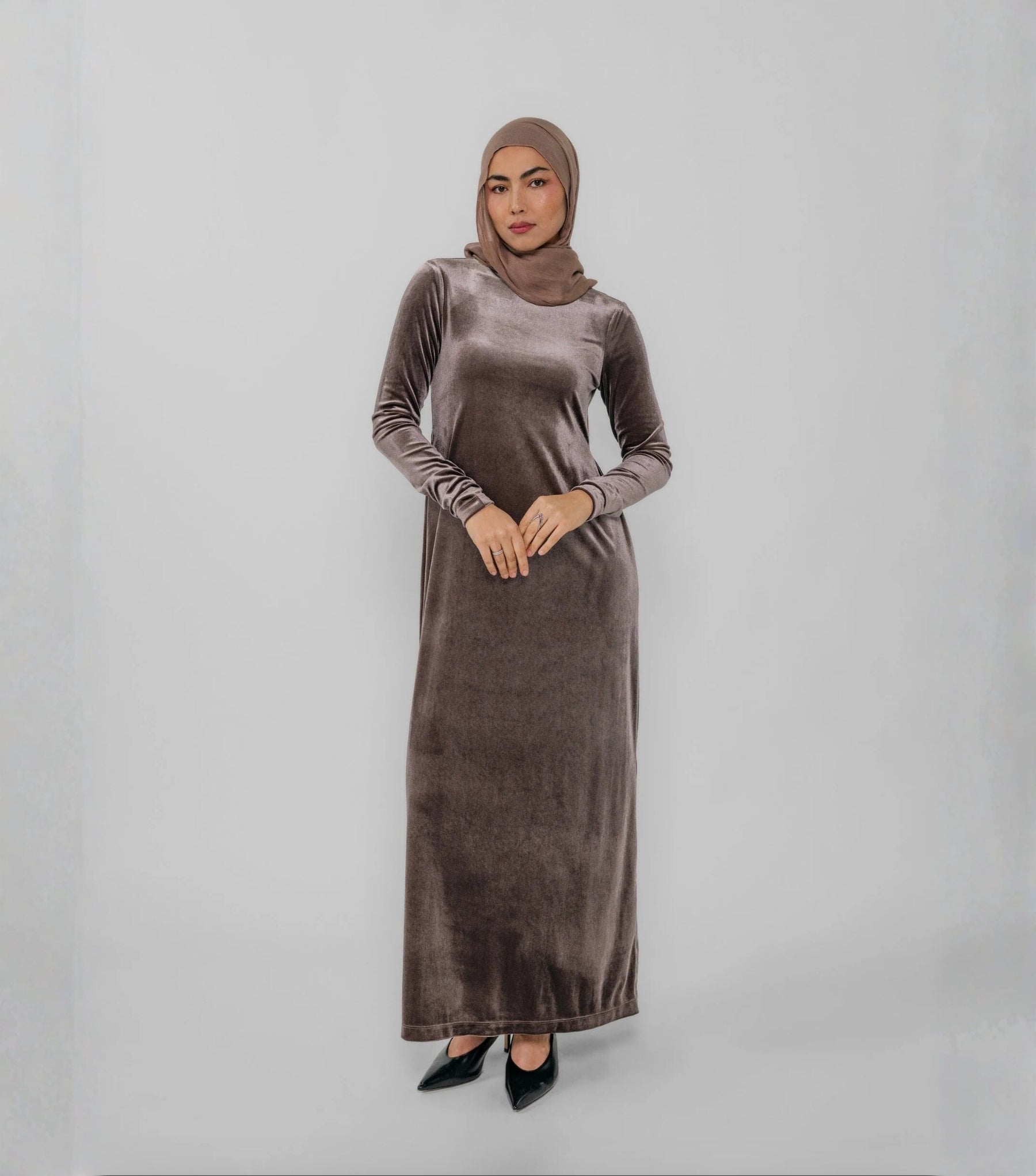 Woman wearing a long brown dress with a hijab on a white background